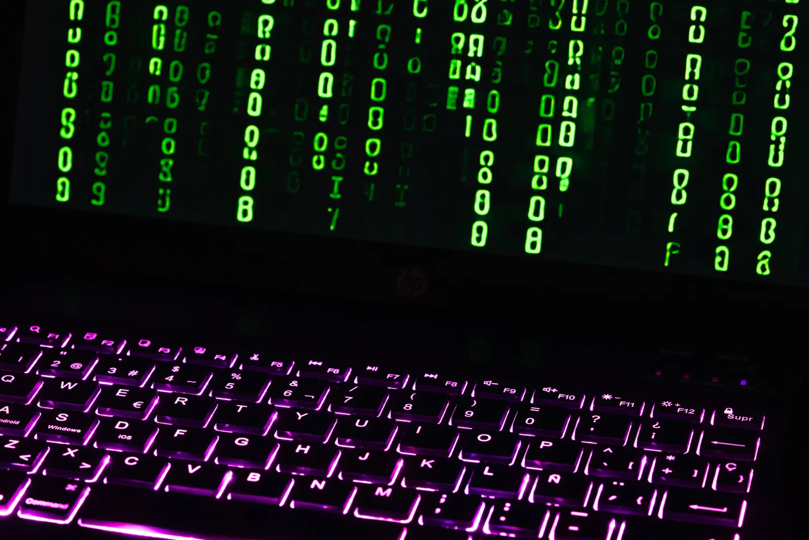 Computadora portátil en la oscuridad con código verde en la pantalla y el teclado iluminado