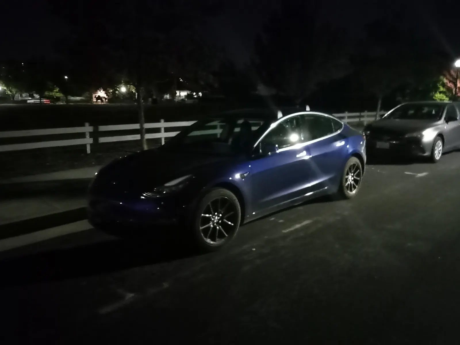 Tesla Model 3 azul estacionado de noche junto a otro auto